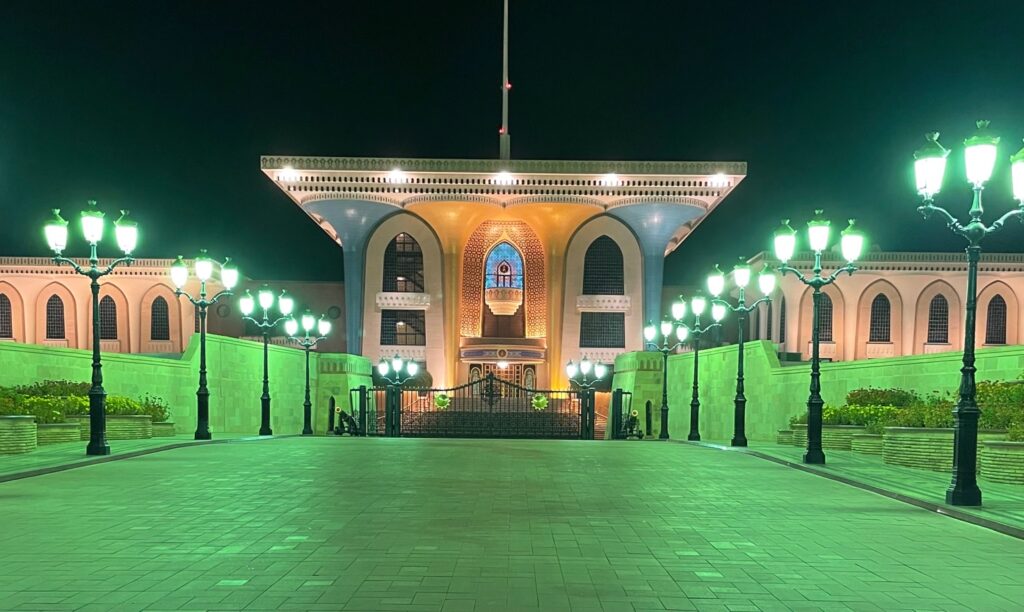 Al Alam Palace at night with a green background, highlighting the blue and yellow palace