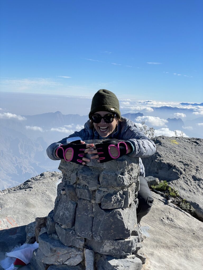 Erin smilles while holding on to the summit stone